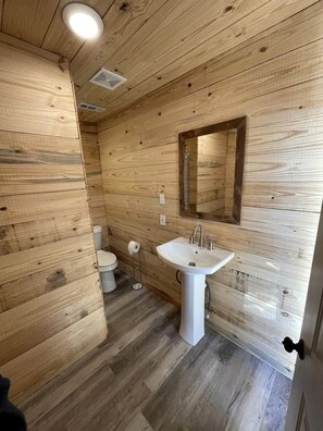 Ein Badezimmer mit Holzwandverkleidung, einem weißen Waschbecken, einem Spiegel und einer Toilette.