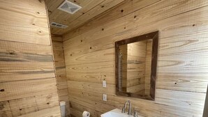 Puupaneloitu kylpyhuone, jossa on valkoinen pesuallas, peili ja wc-istuin.