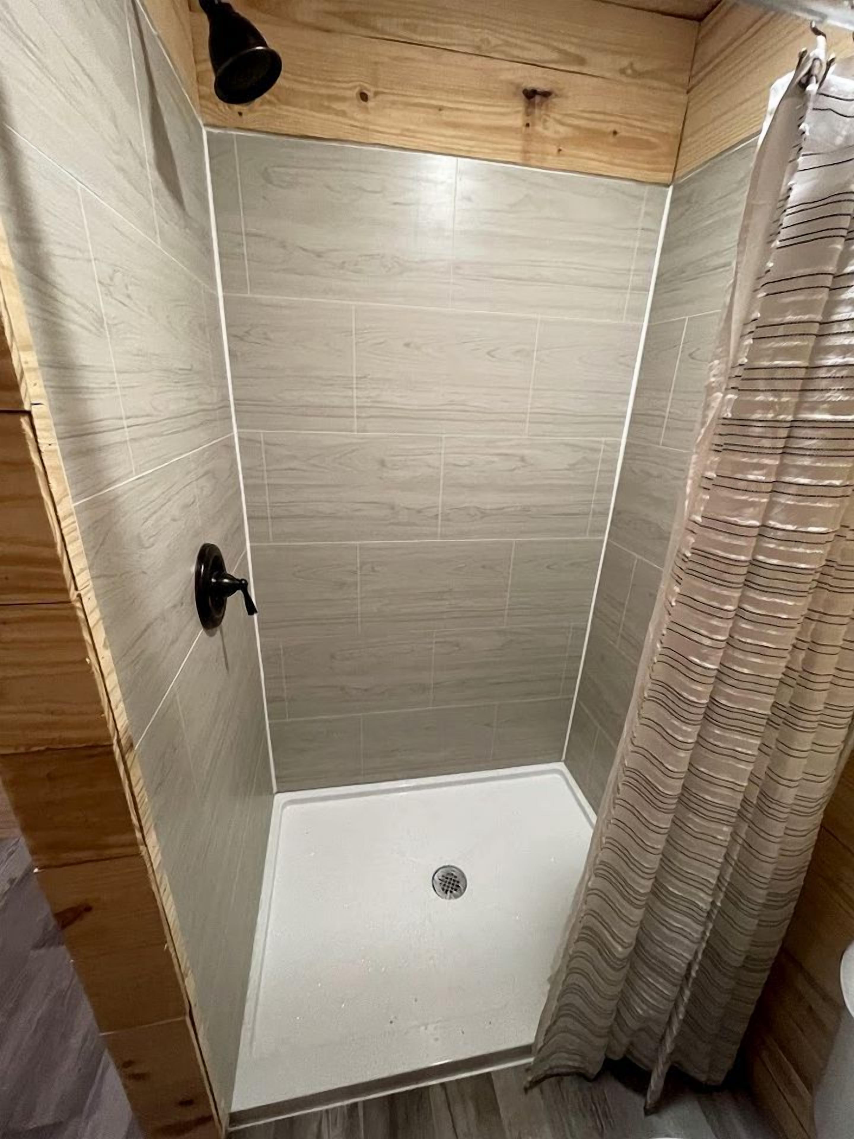 A shower with a drain, wooden walls, and a curtain.