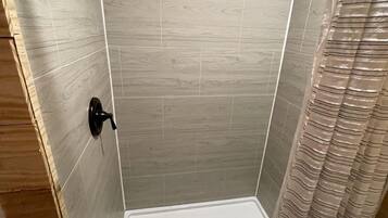 A shower with a drain, wooden walls, and a curtain.