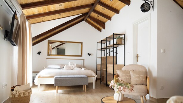 Un dormitorio con cama, un banco, una silla, una mesita, un espejo y un reloj en la pared.