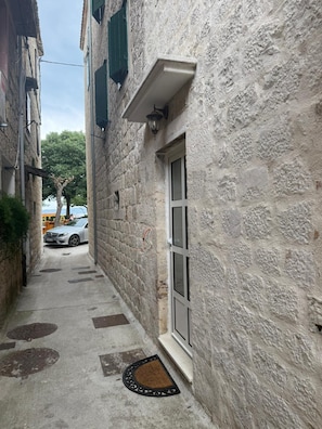 A narrow alleyway with stone walls, a door with a window, and a doormat. - Beautiful studio apartment Milica close to the beach (Kaštel Novi)