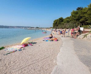 A beach with people sunbathing and swimming, a pebble beach, and a clear blue sky. - Beautiful studio apartment Milica close to the beach (Kaštel Novi)