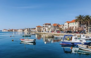 A coastal town with boats docked along the waterfront, stone buildings with red roofs, and a clear blue sky. - Beautiful studio apartment Milica close to the beach (Kaštel Novi)