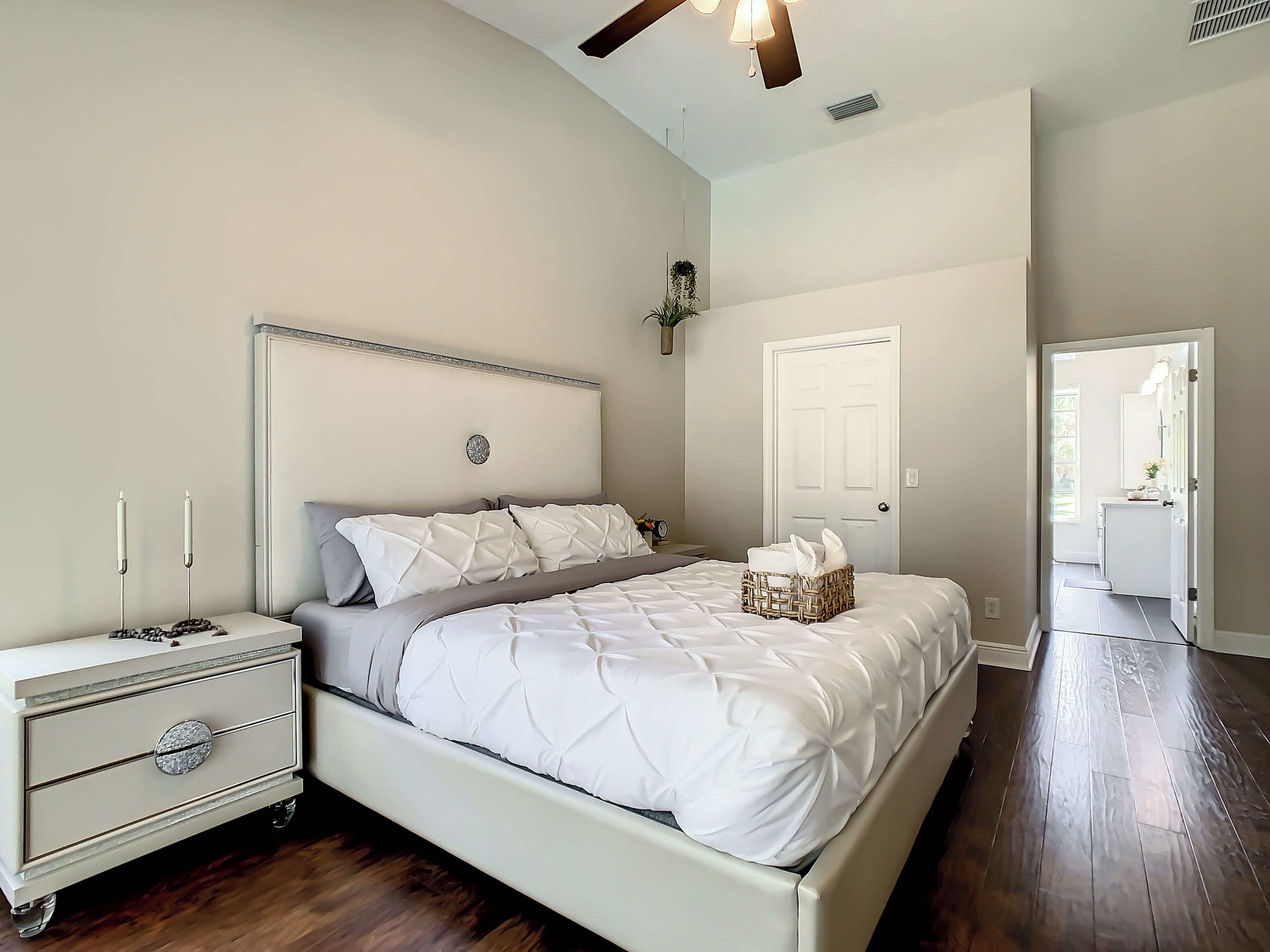 A bedroom with a bed, nightstand, dresser, and a door leading to another room.