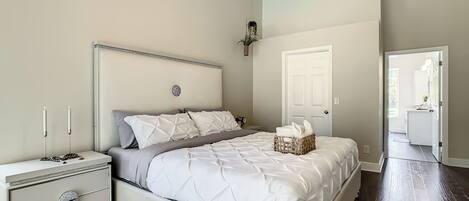 A bedroom with a bed, nightstand, dresser, and a door leading to another room.