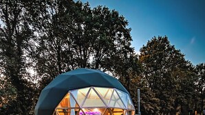 A geodesic dome structure with a transparent roof, surrounded by a gravel area and red flowers in the foreground.