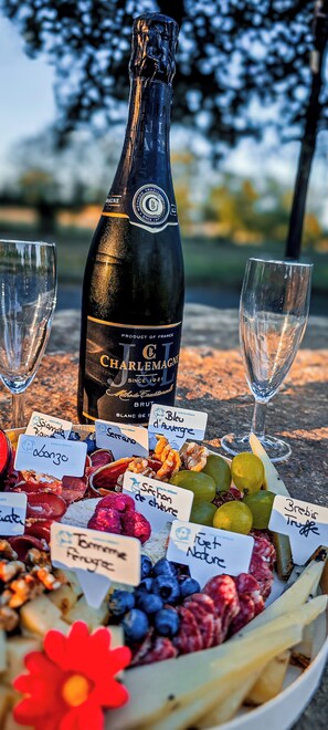A bottle of Charlemagne wine, two empty glasses, and a variety of fruits and nuts on a table.
