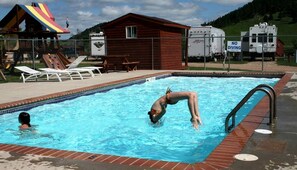 Ein Schwimmbecken mit Sprungbrett, Liegestühlen und einer kleinen Umkleidekabine.