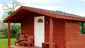 Une petite cabane en bois avec une véranda, une porte et deux chaises en bois.