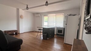 A spacious living area with a sofa, a dining table, and a kitchen with a refrigerator and oven. - Bright Loft Apartment for the Modern Minimalist with A/C, Internet, and Parking (Florești)