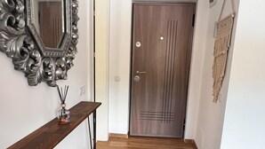 Un corridoio con pavimento in legno, un tavolino consolle con uno specchio, una porta con pannello decorativo e un tappezzeria in macramè.