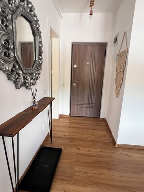 Ein Flur mit Holzboden, einem Konsolentisch mit Spiegel, einer Tür mit dekorativer Verkleidung und einem Wandbehang aus Makramee.