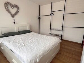 A bedroom with a bed, a heart-shaped decoration, a hanging light, and a black metal shelf unit.