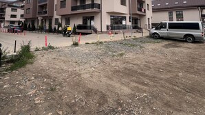 Un edificio residenziale a più piani con balconi, un'area parcheggio e terreno sterrato.