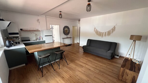 Una cucina moderna con isola centrale, una zona pranzo con divano e un soggiorno illuminato da una lampada da terra.