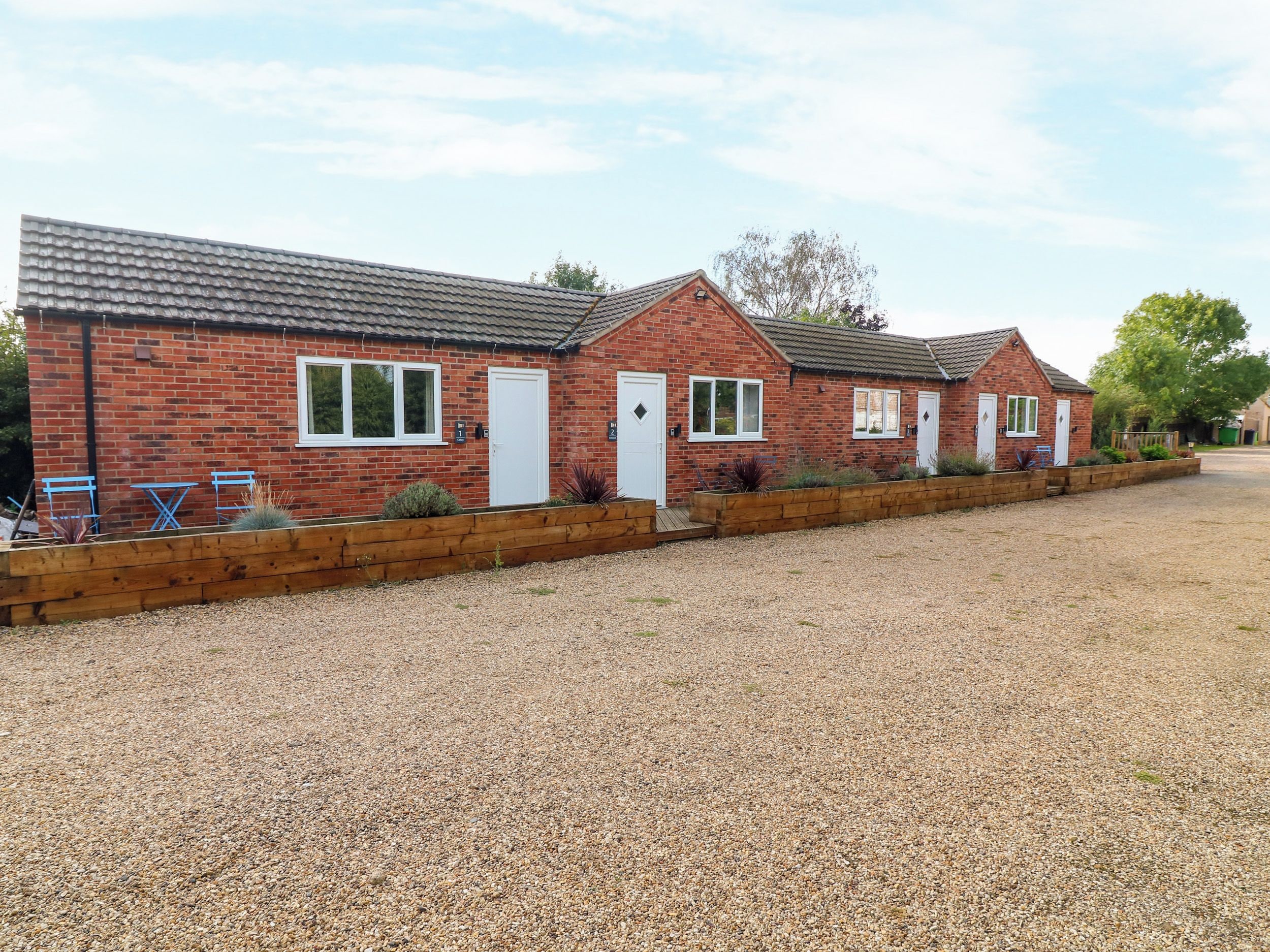 A row of brick houses with white doors and windows, a gravel driveway, and a wooden fence.