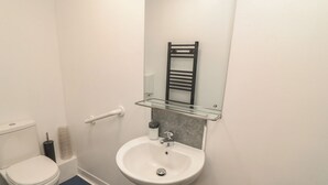 Un baño con inodoro blanco, lavamanos pedestal, repisa de vidrio y toallero.