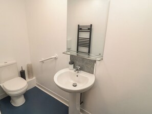 Un baño con inodoro blanco, lavamanos pedestal, repisa de vidrio y toallero.