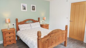 Un dormitorio con una cama de madera, dos mesitas de noche, un tocador, una puerta de madera y dos cuadros enmarcados en la pared.