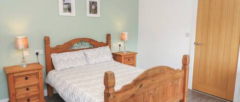 A bedroom with a wooden bed, two bedside tables, a nightstand, a wooden door, and two framed pictures on the wall.