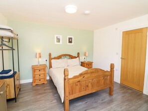 Een slaapkamer met een houten bed, twee nachtkastjes, een kledingkast van hout en een houten deur.