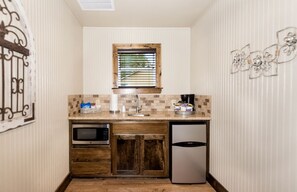 A compact kitchen with a microwave, oven, and refrigerator, a window with blinds, and a wooden cabinet. - Relaxing Fredericksburg Hill Country Cottages with Porch Swings & Private Wine Collective Access in Texas (Fredericksburg)