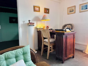 A cozy room with a desk, chair, lamp, and framed pictures on the wall.