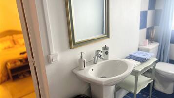 Et badeværelse med en hvid vask, et spejl, et toilet og en håndklædestang.