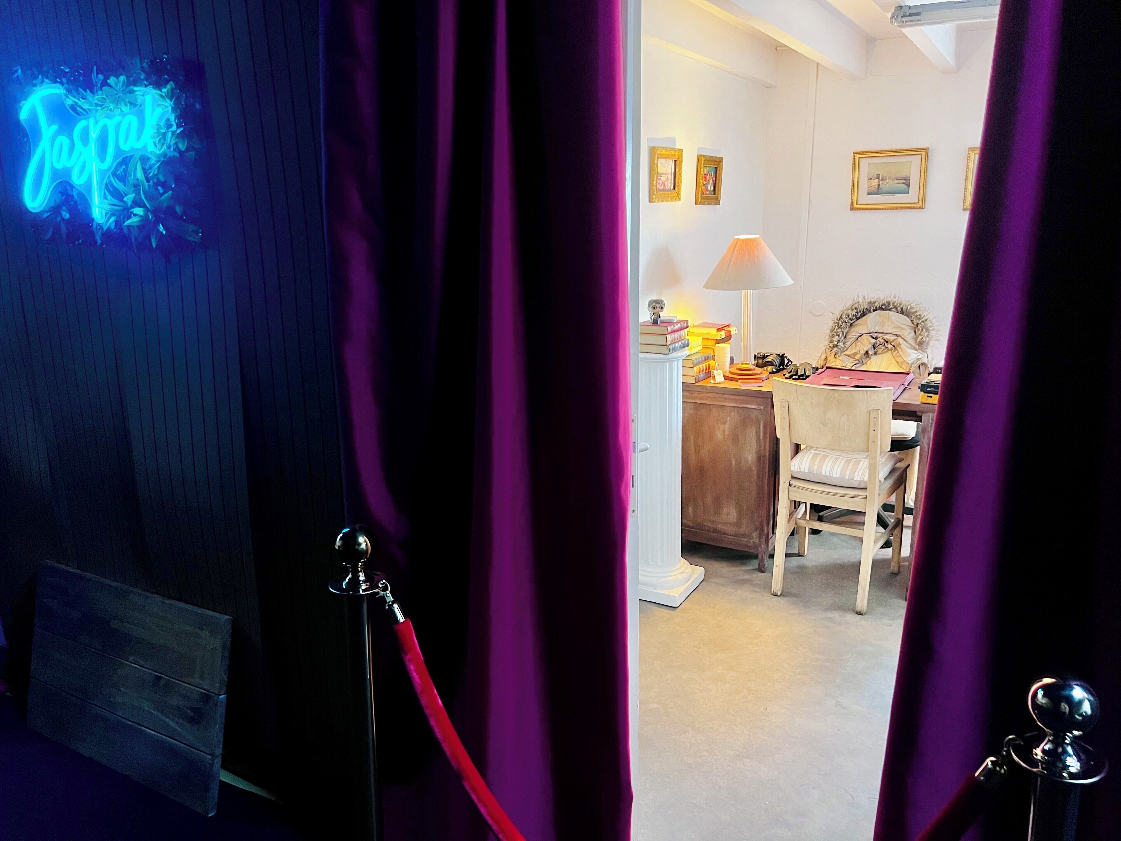 A room with a desk, chair, lamp, and framed pictures on the wall.