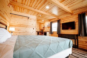 Une chambre dans un chalet en bois, équipée d’un lit, d’une télévision, d’un bureau et d’une fenêtre.