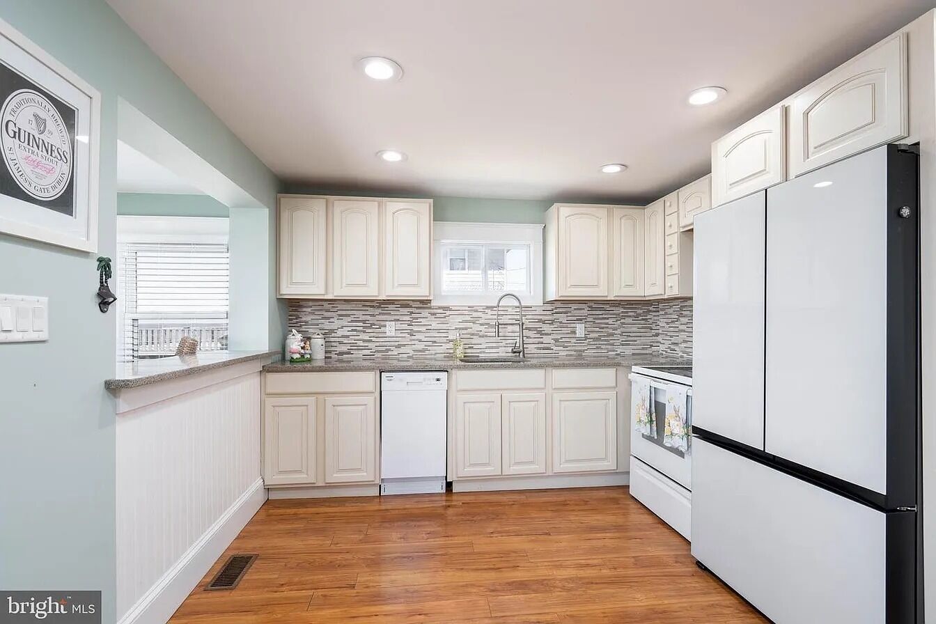 A kitchen with white cabinets, a dishwasher, a refrigerator, and a window with blinds.