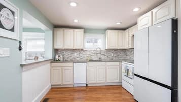 A kitchen with white cabinets, a dishwasher, a refrigerator, and a window with blinds.