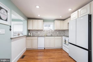 A kitchen with white cabinets, a dishwasher, a refrigerator, and a window with blinds.
