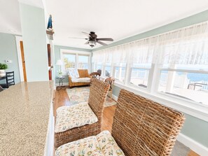 A room with a large window, wicker furniture, a ceiling fan, and a view of the sea.
