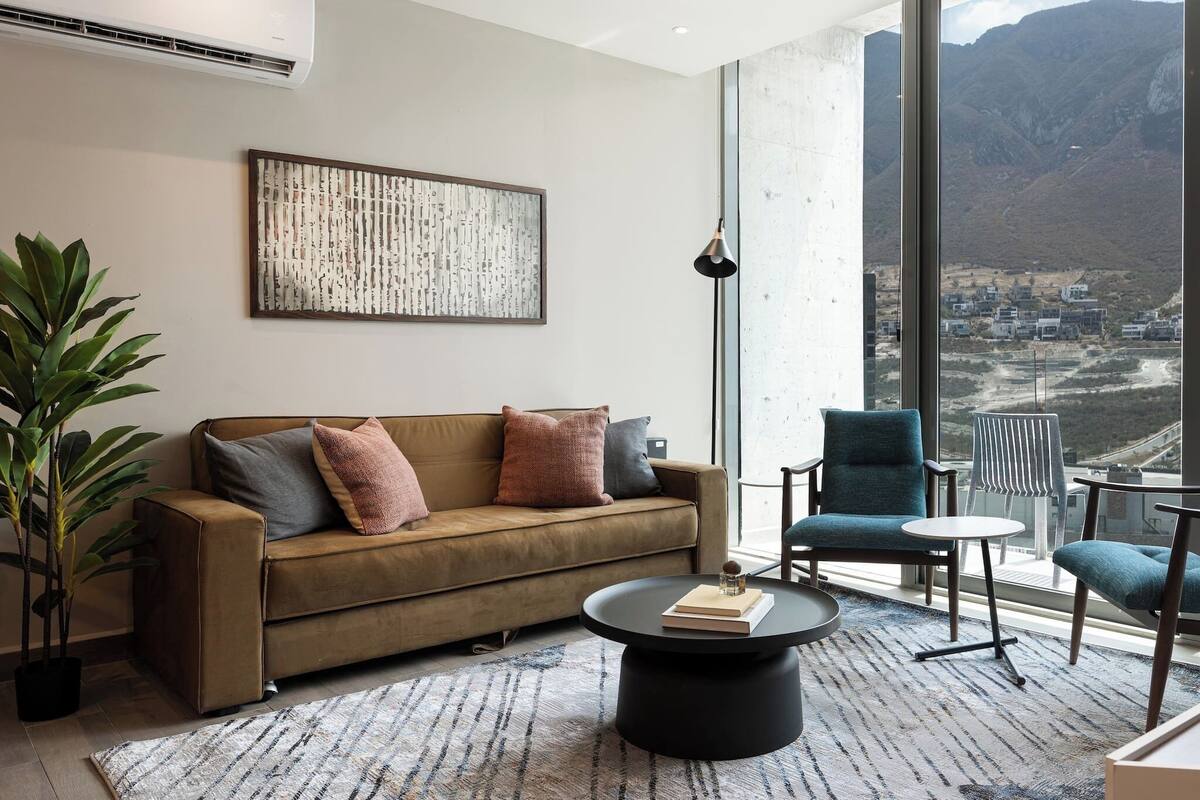 Una sala de estar moderna con un sofá, sillones, una mesa de centro y un ventanal con vistas a la montaña.