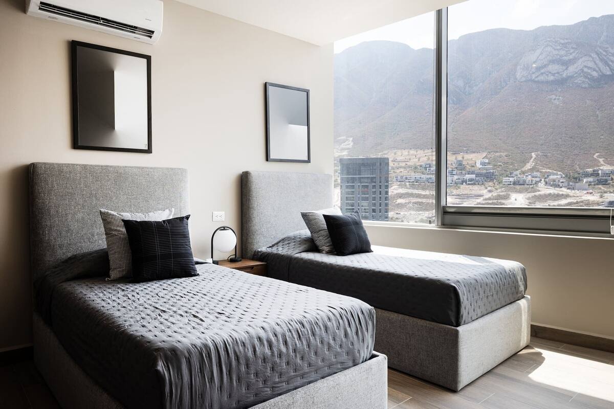 Habitación de hotel con dos camas, un ventanal con vistas a la montaña y un cuadro en la pared.