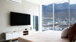 Une chambre avec un grand lit, un téléviseur fixé au mur, une armoire blanche et une fenêtre donnant sur la montagne.