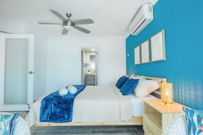 Een slaapkamer met een bed, een plafondventilator, een airconditioner, een nachtkastje met een lamp en een deur.