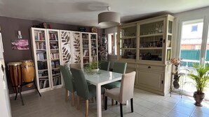 Uma área de refeições com uma mesa de vidro, cadeiras verdes, um armário branco com portas de vidro e uma planta em vaso.