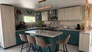 Uma cozinha moderna com uma ilha central, banquetas e um lustre pendente.