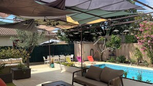 Uma área de pátio com móveis de exterior, piscina e guarda-sóis para sombra.