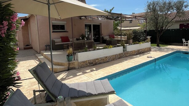 Uma piscina com espreguiçadeiras e um guarda-sol, uma área de estar com móveis de exterior e um edifício com telhado em azulejo.