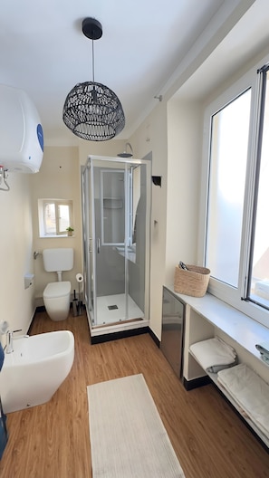 Un bagno moderno con box doccia in vetro, lavandino bianco e un'ampia finestra.