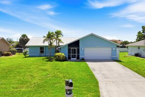 A residential house with a garage, a lawn, and a clear sky. - Low Key Tiki (Cape Coral)