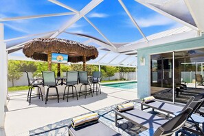 A covered outdoor area with a pool, lounge chairs, and a table with chairs. - Low Key Tiki (Cape Coral)