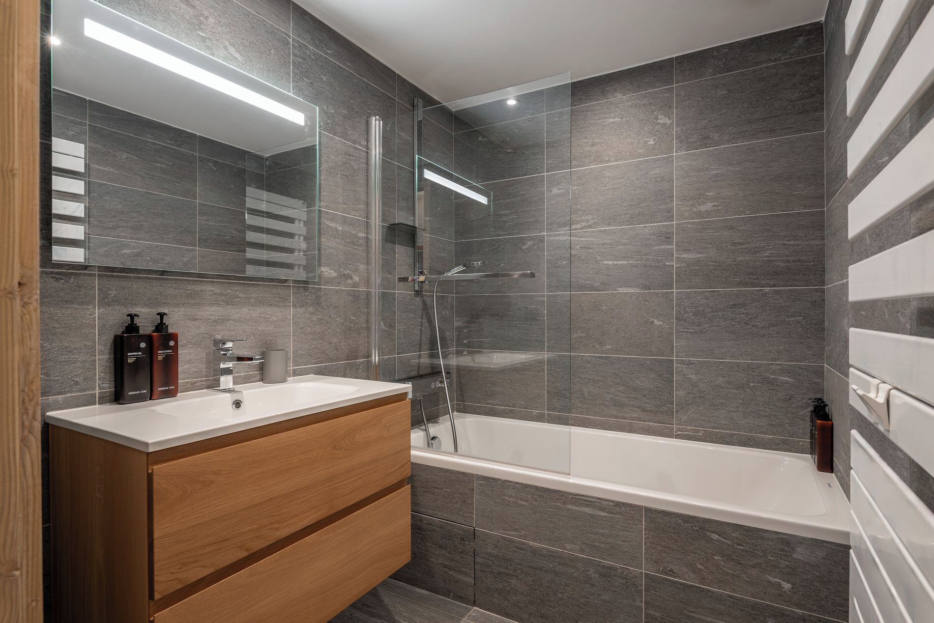 A modern bathroom with a wooden vanity, a glass shower enclosure, and a large bathtub.