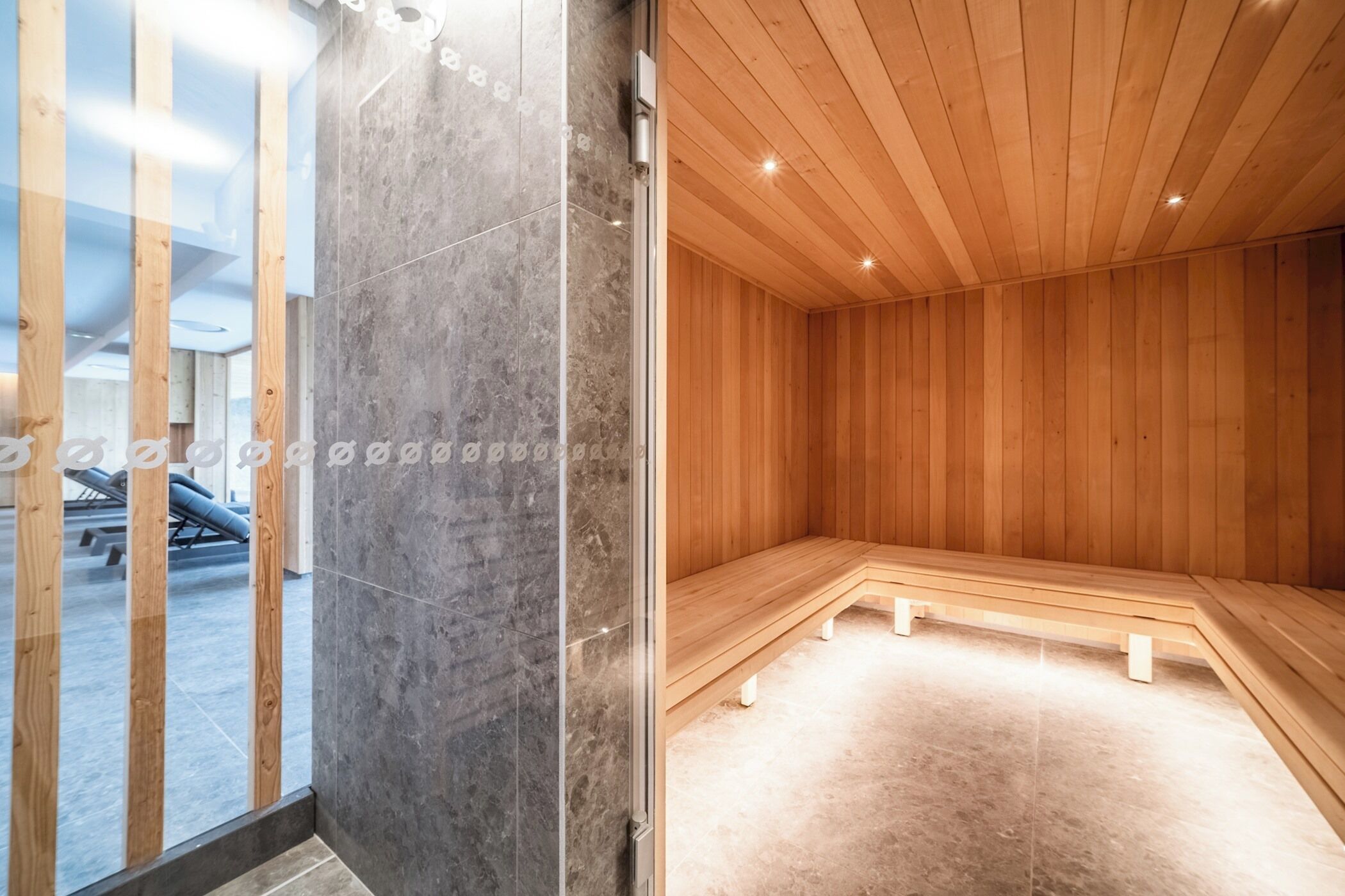 A sauna room with wooden walls and benches, a tiled floor, and a glass door leading to an outdoor area with exercise equipment.