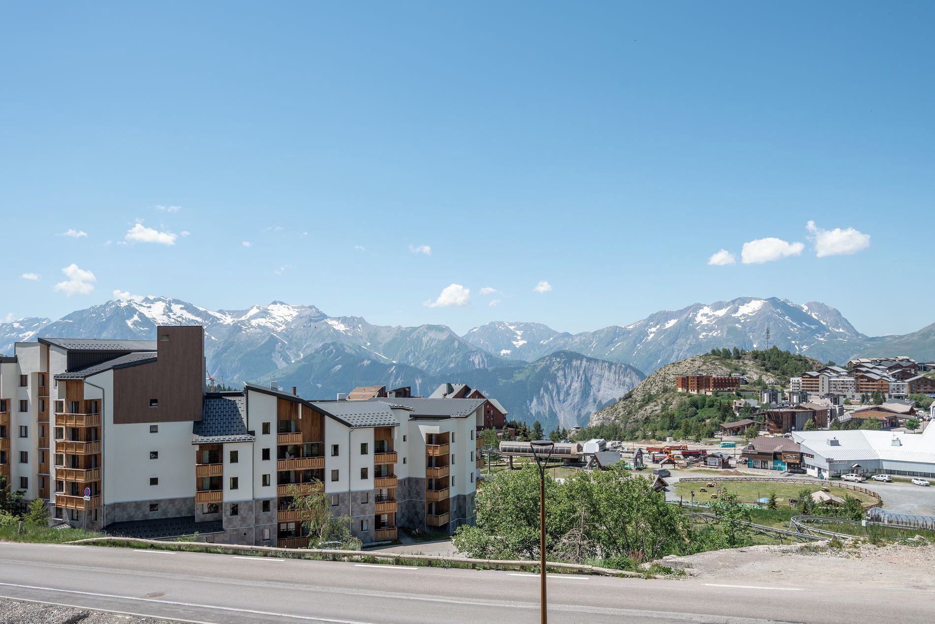 Un edificio moderno con diversi balconi, una strada sullo sfondo e montagne all'orizzonte.