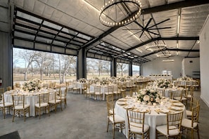 Un espace intérieur vaste et lumineux, avec des tables et des chaises rondes, de grandes fenêtres et un plafond haut.